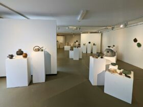 A photo of inside an art gallery. Olive floors, white walls, and handmade ceramics on white plinths
