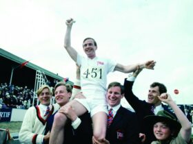Still from Chariots of Fire showing a group of men cheering. One man is on the shoulders of another.
