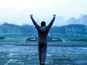Still from Rocky showing a man with fists raised facing a cityscape in winter