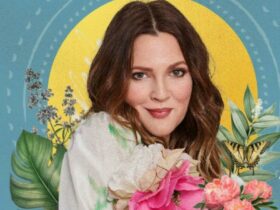 Photo of Drew covered in plants and flowers with a smile on her face behind a blue background.