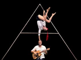 a performer with red hair doing a handstand on a musician's head