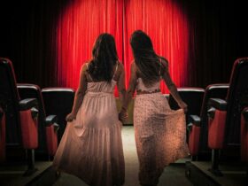 Two feminine people holding hands and hoisting their skirts as they walk down the aisle of a theatre