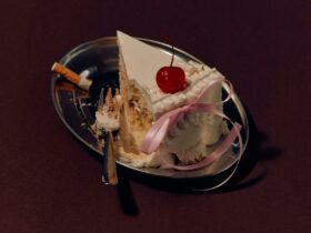 A silver tray with a slice of cake, a fork, and a cigarette.